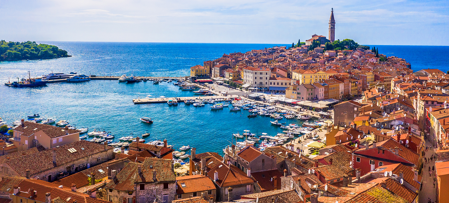 Luftaufnahme der Altstadt von Rovinj auf ihrer Halbinsel mit dem Glockenturm der Kirche der heiligen Euphemia über einem Hafen voller Boote