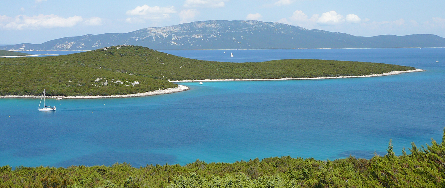 Segelyacht vor Anker in einer türkisfarbenen Bucht vor Unije, dahinter eine höhere Insel